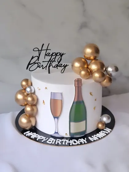 A simple and elegant cake for a special celebration, featuring a champagne bottle and glass, accented with gold and silver spheres.
