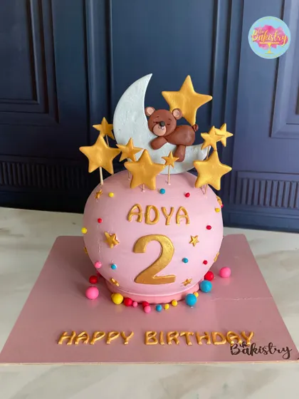 A full view of the whimsical pink sphere cake for Adya's 2nd birthday, topped with a teddy on the moon.