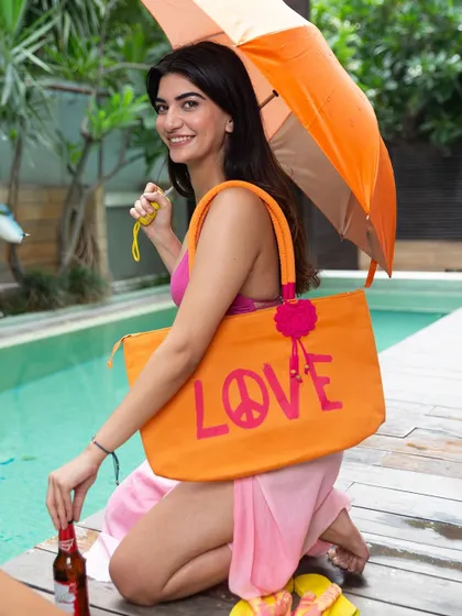 A fun and vibrant poolside photo for the brand Beachbum, featuring a model with a large "LOVE" tote bag. This image is full of color and energy, ideal for a summer social media campaign.