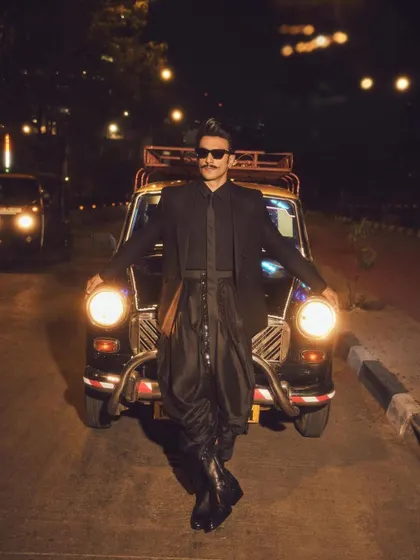 A wide shot of Ranveer with the iconic kaali-peeli taxi. The styling was designed to be both high-fashion and grounded in a cool, urban Mumbai context.