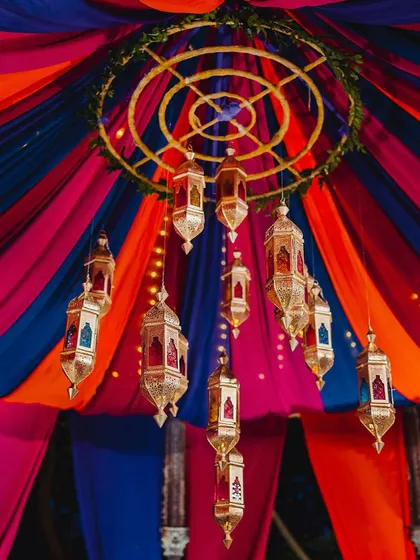 A stunning chandelier made of Moroccan lanterns hangs from the center of a colorful draped ceiling, creating a magnificent focal point for the Sangeet.