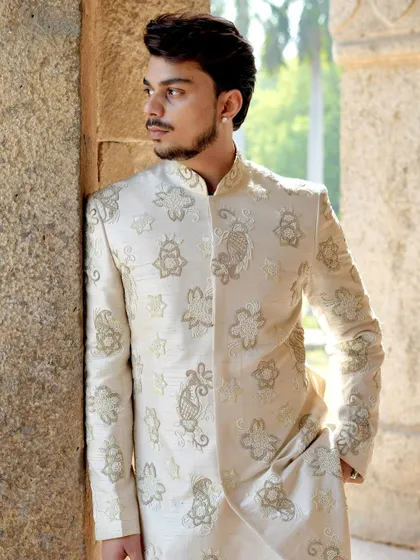 A close-up portrait highlighting the detailed embroidery around the collar and chest of the ivory sherwani. This is where traditional craftsmanship meets modern sophistication.