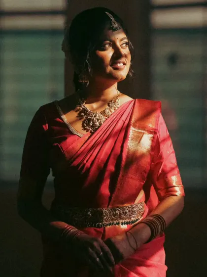 A sunlit portrait of a bride in a red saree. The light filtering through the window creates a warm, nostalgic glow, perfectly matching my vintage photography style.