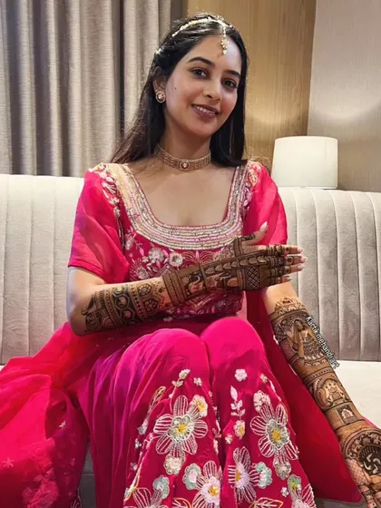 A happy bride proudly displaying her full-arm mehandi. The design is a beautiful mix of portraits and traditional patterns.