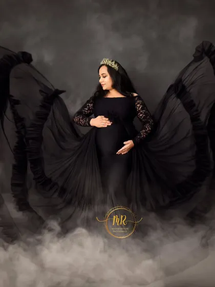 A glamorous solo maternity portrait in a black lace-sleeve gown. The flowing fabric and misty effect at the bottom create a dramatic and enchanting look.