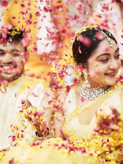 The couple smiling as they are showered with pink and yellow petals, perfectly matching their outfits and the decor.