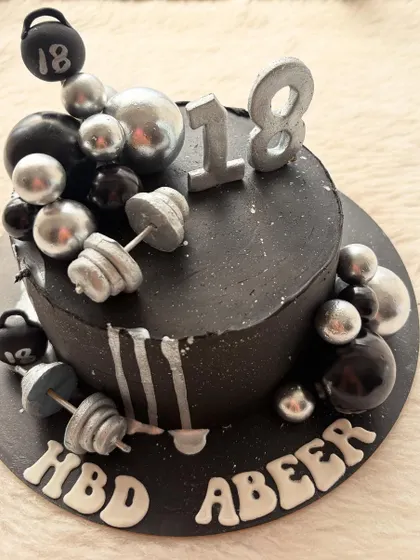 A gym-themed cake for an 18th birthday. The all-black design is decorated with silver dumbbells, kettlebells, and weights for a strong and stylish look.