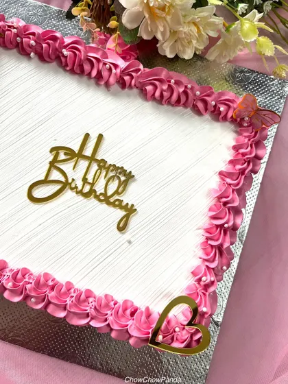A close-up of the piped border on a simple and elegant birthday sheet cake. The pink rosettes and edible pearls add a classic touch.