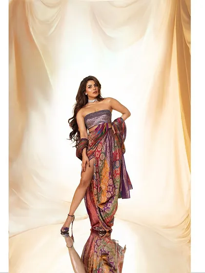 A studio portrait of Priyanka Chopra, styled in a draped, multi-patterned ensemble. The lighting is designed to sculpt her form and highlight the rich textures of the fabric, creating a regal and powerful image.