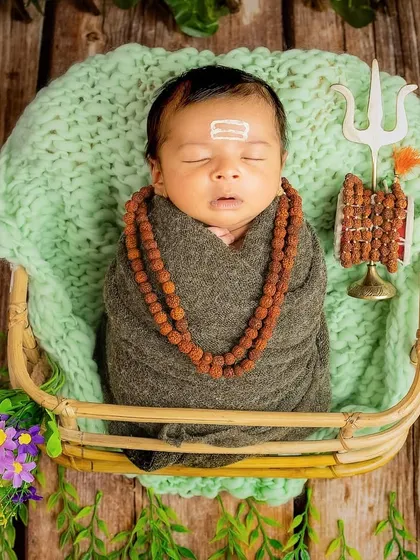 A beautiful portrait of a newborn in a Mahadev-themed setup. The baby is nestled in a basket, surrounded by elements like the Trishul and Damaru, creating a complete and artistic scene.