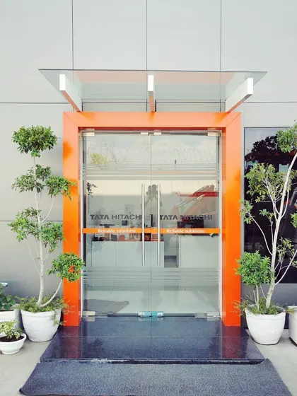 The primary entrance door, framed in the brand's signature orange. This detail reinforces the corporate identity from the moment of arrival and is flanked by manicured plants in modern planters.