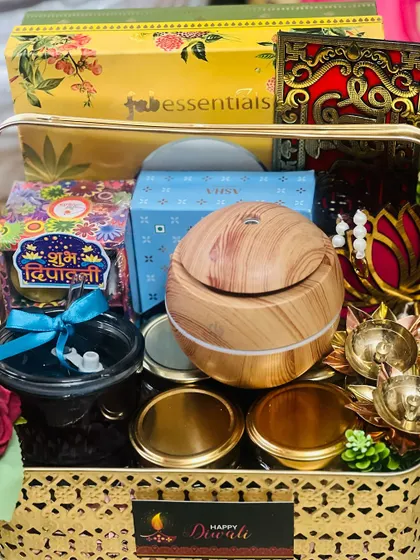 A golden metal basket filled with Diwali goodies, including an aroma diffuser, diyas, and jars of sweets and nuts. A perfect blend of modern wellness and traditional celebration.