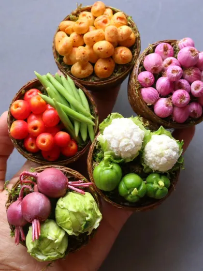 A hand holding five baskets of miniature vegetables, showcasing their tiny scale and vibrant colors.