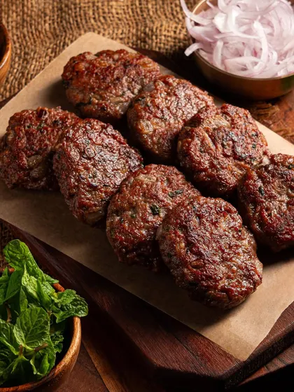 A platter of perfectly seared Galouti kebabs. The focus is on the texture and color of the meat, making it look incredibly appetizing.