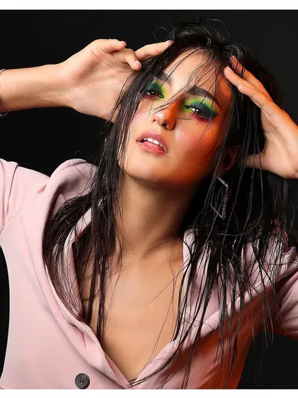A close-up of the wet-look editorial, focusing on the vibrant green and yellow eye makeup. The model's expression is powerful and captivating.