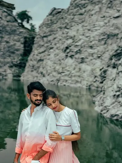 A quiet, intimate moment as a couple embraces by a still lake, with the reflection of the rock face in the water. A peaceful and romantic shot.