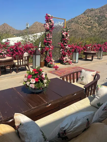 A cozy seating area for a mehendi, with a floral photo backdrop set against the stunning Aravali Hills in Udaipur.