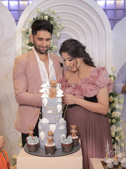 A heartwarming moment as the parents-to-be cut their cake at an elegant, all-white baby shower. The teddy bear-themed cake and sophisticated backdrop create a beautiful memory.