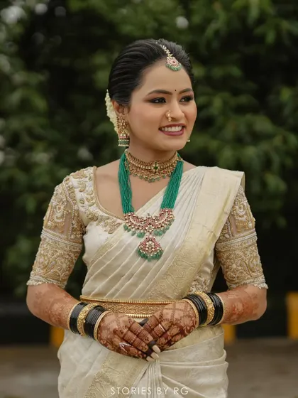 A smiling portrait of Harshitha, her traditional South Indian bridal look perfected with green beaded jewelry.
