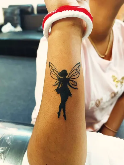A solid black silhouette of a fairy on the forearm. This design combines minimalist principles with a touch of fantasy.