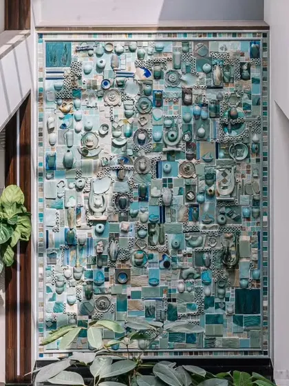 A full view of the magnificent turquoise ceramic mural. It's a vibrant puzzle of textures, shapes, and shades of blue, celebrating the beauty of everyday objects through the medium of pottery.