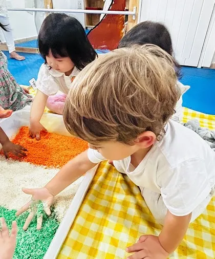 Children explore a sensory bin filled with rice colored saffron, white, and green for Independence Day.