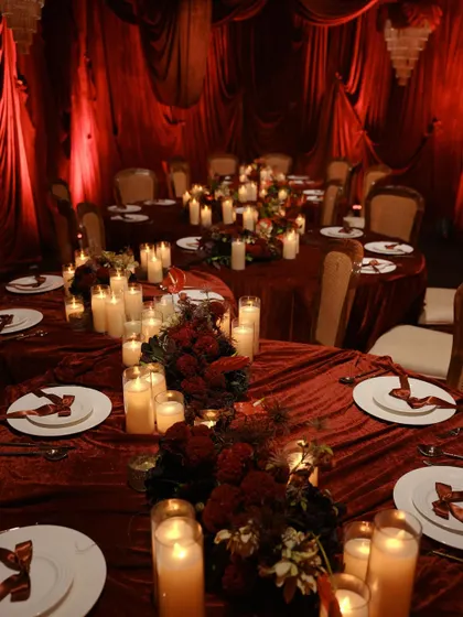 A full view of the elegantly set dining tables. The white plates provide a crisp contrast to the deep red of the linens and floral arrangements.