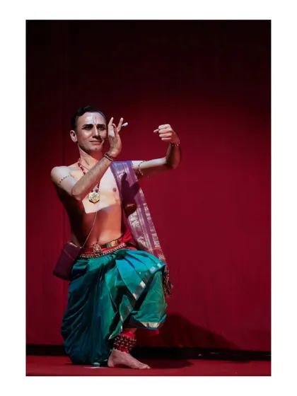 A moment of expressive storytelling from "Tyāgarāja Hṛt Sādana." The vibrant red background enhances the emotional intensity of the scene.
