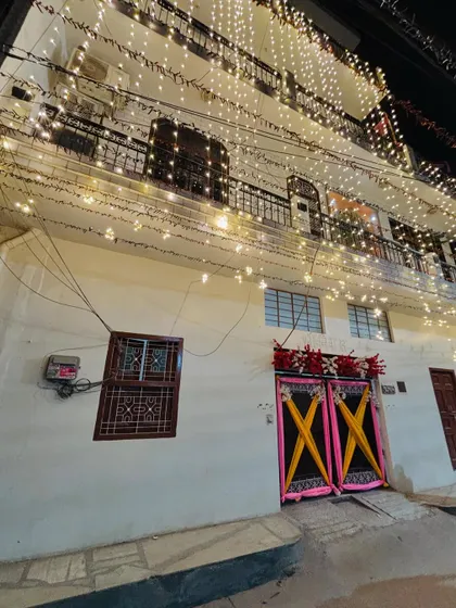 A wedding house decorated for a Haldi ceremony. The facade is covered in fairy lights, and the entrance gate is decorated with colorful drapes.