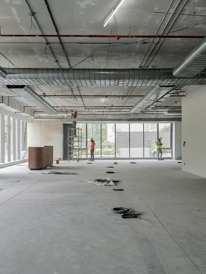 A wide shot of a raw construction site, showing the exposed ceiling, ductwork, and vast open floor before the final finishes are applied.