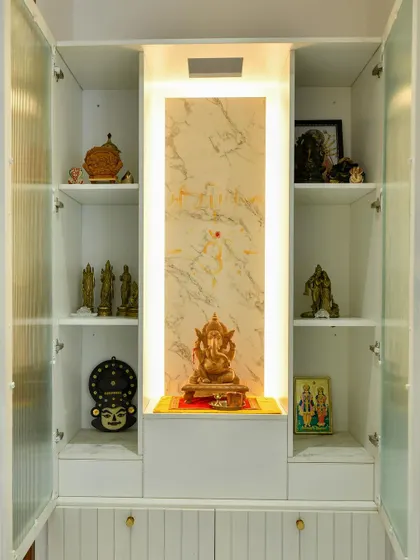 A clean and elegant pooja unit with fluted glass doors, a marble-clad niche for the main idol, and ample shelving for other sacred items, all illuminated with soft, respectful lighting.