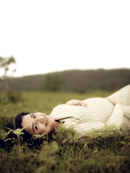 A lovely shot of the mom-to-be lying in the grass, looking up at the camera with a gentle smile. The low angle and natural foreground create a very intimate feel.