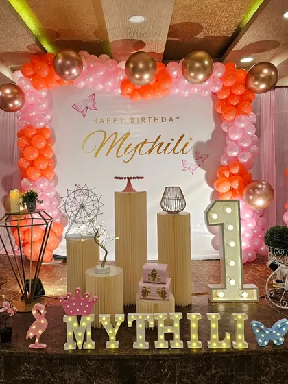 A sweet first birthday setup with an orange and pink color scheme, featuring a large "ONE" and personalized name sign.