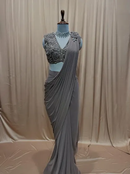 A classic drape saree in a subtle grey tone, paired with a sleeveless blouse fully embroidered with intricate floral patterns.