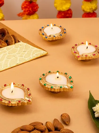 A set of four ornate, jewel-toned diyas. The warm lighting and festive props like dry fruits and flowers create a rich and inviting scene.