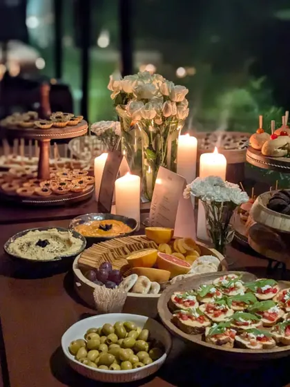 An intimate and moody grazing table illuminated by candlelight. This setup features an array of gourmet delights including bruschetta, olives, hummus, and a cheese board, creating a warm and inviting ambiance for an evening gathering.