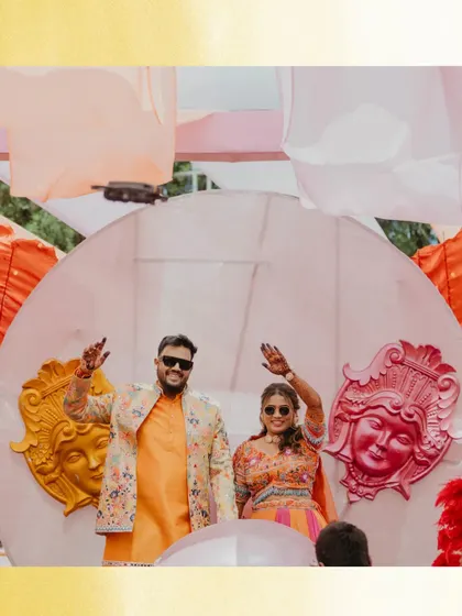 The couple makes a grand entrance at their Haldi carnival. Their waving hands and the fun, quirky decor in the background capture the festive and celebratory atmosphere.