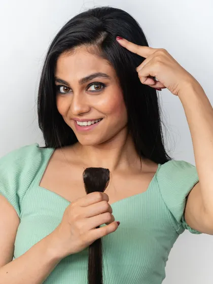 A model holding a side bang extension, pointing to where it can be placed to add volume or a splash of style. These are fully customizable to match your hair.