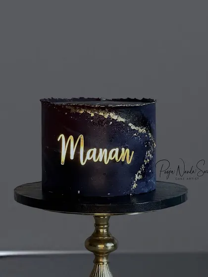 A simple and elegant gold acrylic name charm on a dark, moody cake. The contrast makes the name pop, creating a sophisticated and personalized look.