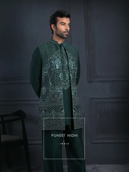 An emerald kurta set paired with a sleeveless embroidered jacket. Subtle geometric patterns and paisley accents flow across the rich green fabric, reflecting understated luxury.