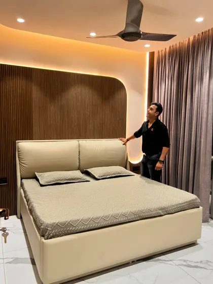 A completed bedroom featuring a bed with a cushioned headboard set against a fluted wood panel wall with curved edges and cove lighting.
