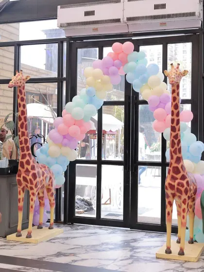 A welcoming entrance to a pastel-themed party, featuring two life-sized giraffe props standing guard under a beautiful pastel rainbow balloon arch. This creates an unforgettable first impression for guests.