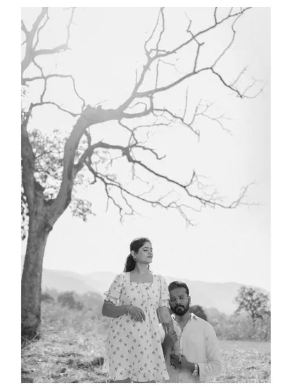 An artistic black and white photo of a couple under a bare, sculptural tree. This high-contrast, minimalist shot focuses on their connection and the beauty of the natural forms around them.