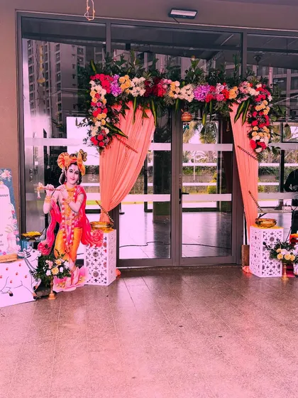 I designed this beautiful entrance for a Janmashtami pooja. The decor features a floral arch with peach-colored drapes, a Krishna cutout, and a personalized welcome sign.