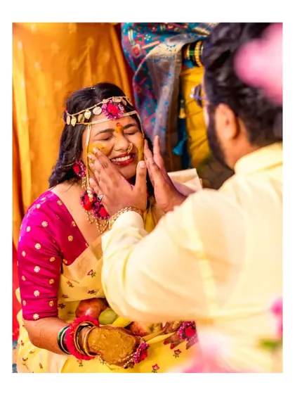 A sweet moment where the groom gently applies Haldi to the bride's face, captured up close to show her blissful expression.