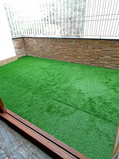 This enclosed balcony now features a perfectly fitted artificial lawn. The turf is cut precisely to fit the space, creating a clean edge against the walls.