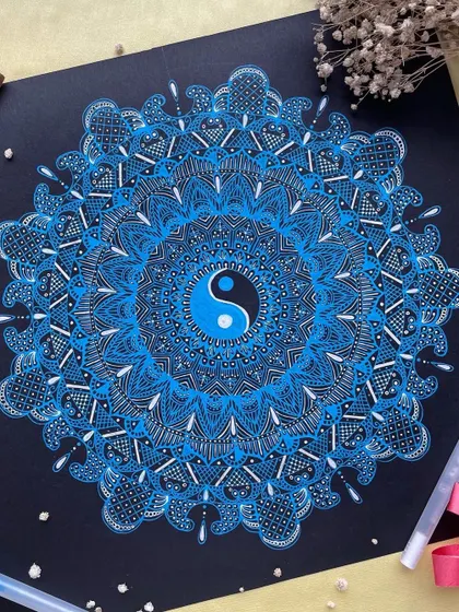 This 12-inch mandala features a yin-yang at its center, created with vibrant blue Gelly Roll pens. The design radiates a sense of balance and cosmic energy.