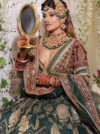 A bride admiring her reflection in our green and maroon velvet lehenga, a timeless and regal choice.