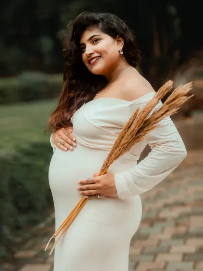 A graceful side-profile portrait of the mother-to-be, holding dried wheat stalks that add a rustic and natural element to the photograph.