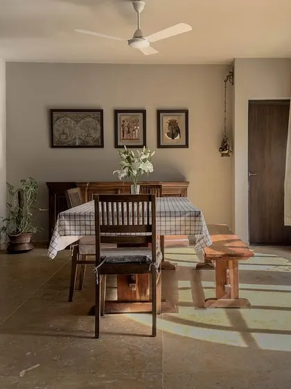 The dining room features a large window with a built-in bay seat, creating a perfect reading nook. Sunlight streams in, illuminating the Jaisalmer stone floor and simple, elegant wooden furniture.